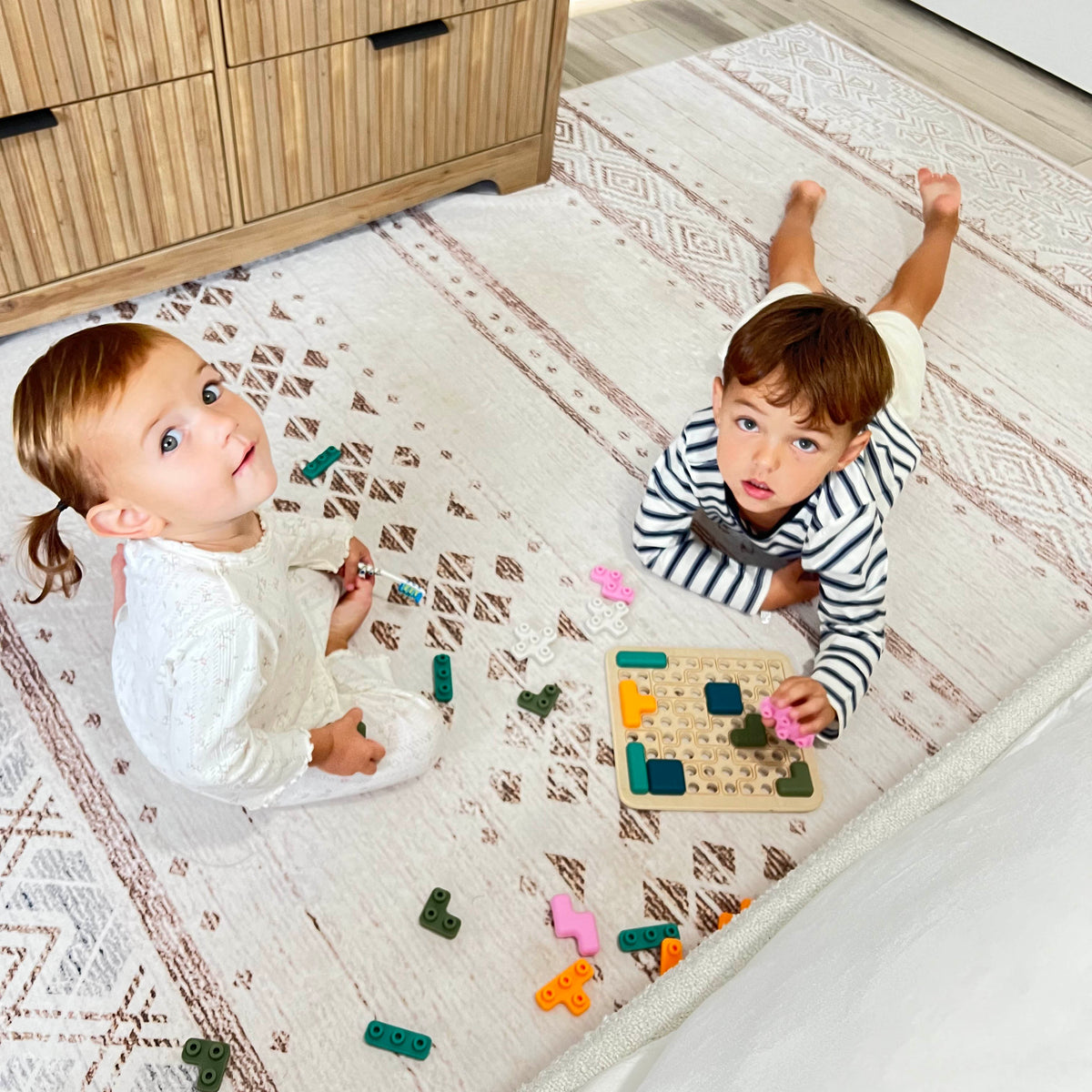 Two children playing with toys on a patterned rug in a room.