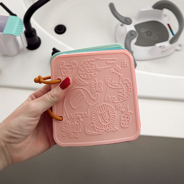 Pink silicone mold with animal designs held by a hand, with a kitchen sink in the background.
