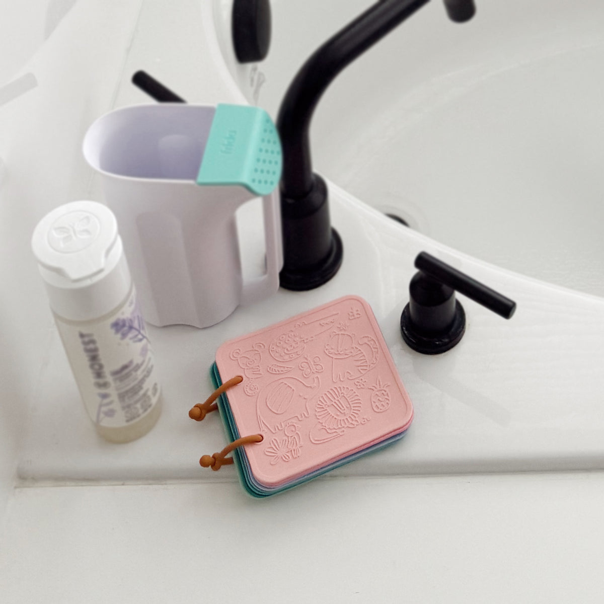Pink soap dish with brown accents on a white surface next to a bottle of soap and a faucet.