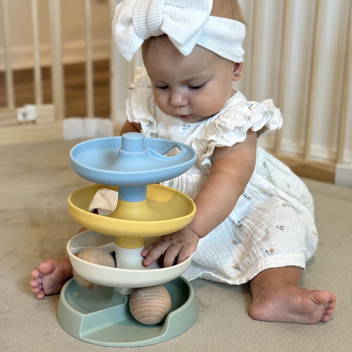Baby playing with a colorful tiered toy on a wooden floor.