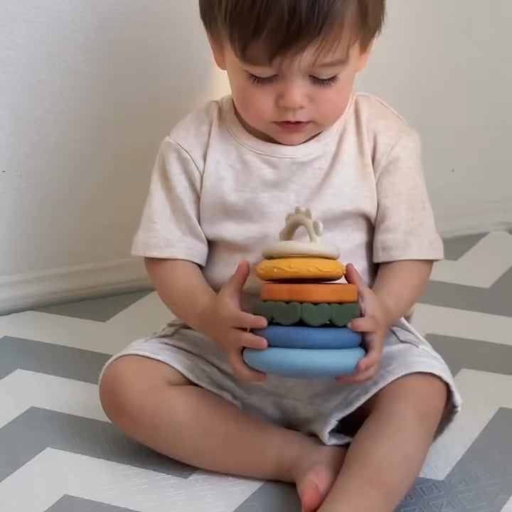 Child holding a stack of colorful rings on a patterned floor.