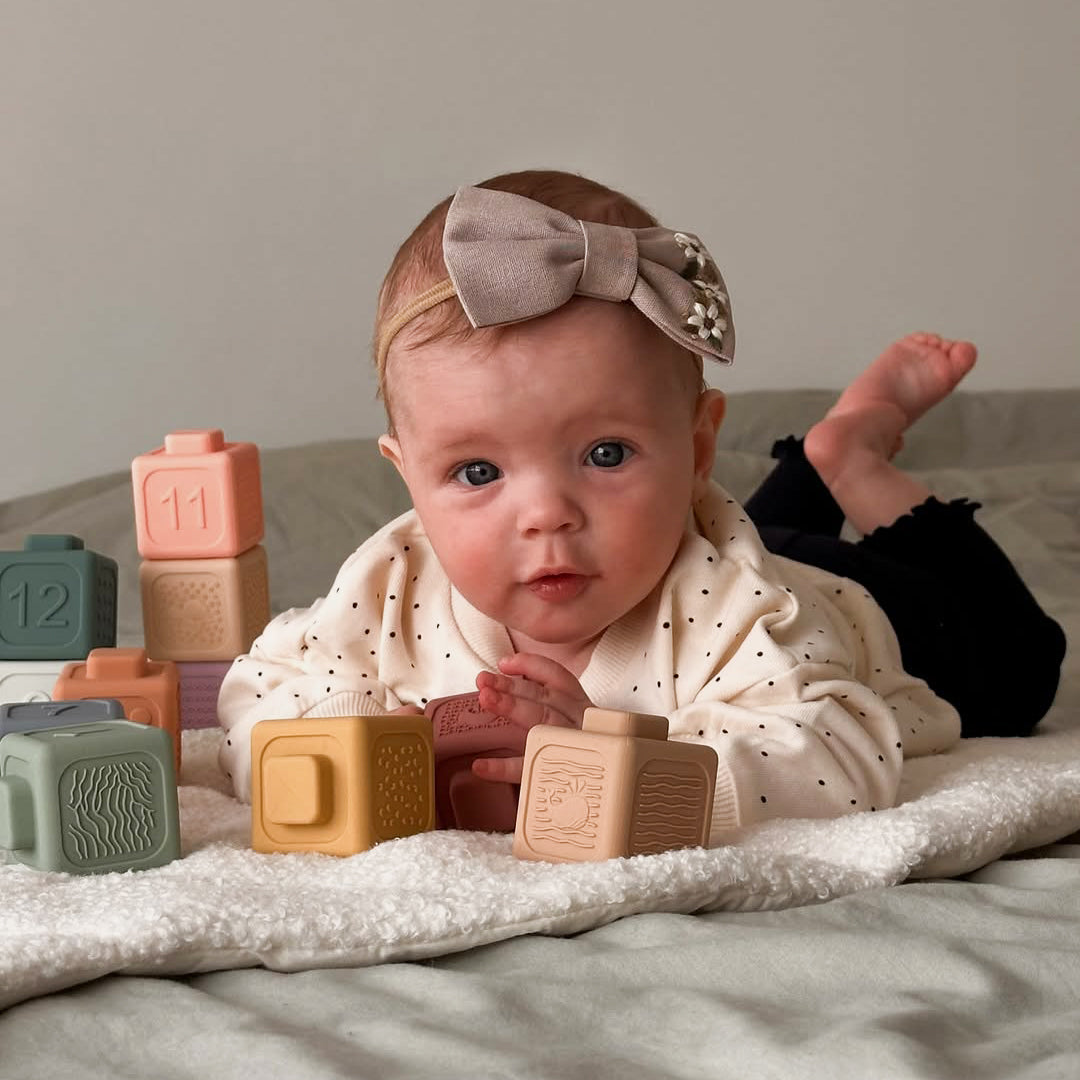 Baby with toys on a blanket, wearing a headband