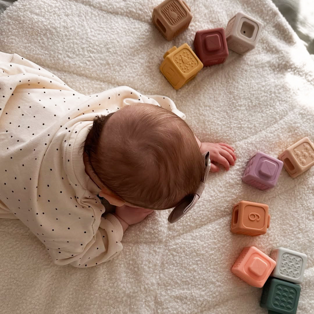 Baby lying on a soft surface with colorful blocks around