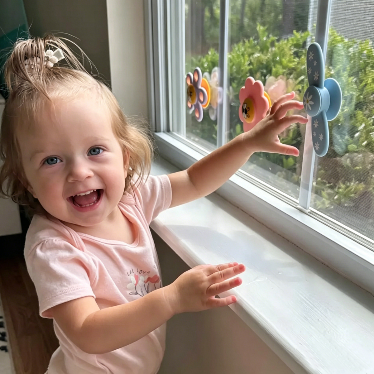 Child by a window with decorative flowers and a view of greenery outside 