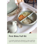 A baby feeding set displayed on a high chair tray, including a divided plate with food, a small teapot, spoons, and a bib. Text at the bottom reads 'First Bites Full Kit' with a descriptive subtitle.