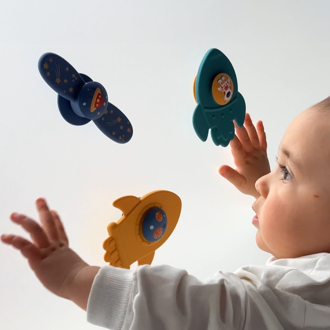 Baby reaching out towards colorful toy vehicles on a white background 