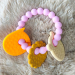 Teething ring with pink beads and various textures on a fluffy surface 