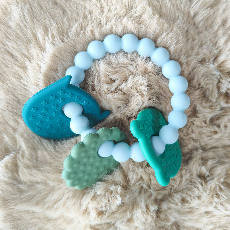 Teething toy with blue, green, and white beads on a fluffy beige surface 