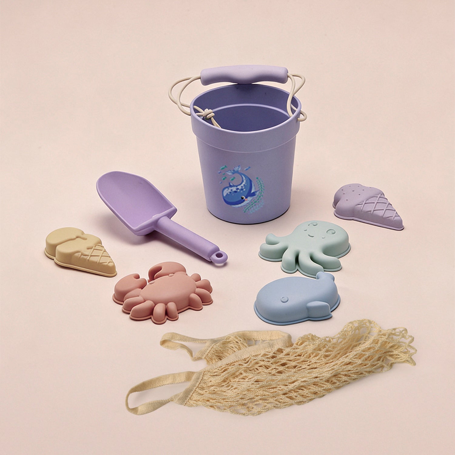 Set of children's sand toys including a bucket, shovels, and molds on a beige background