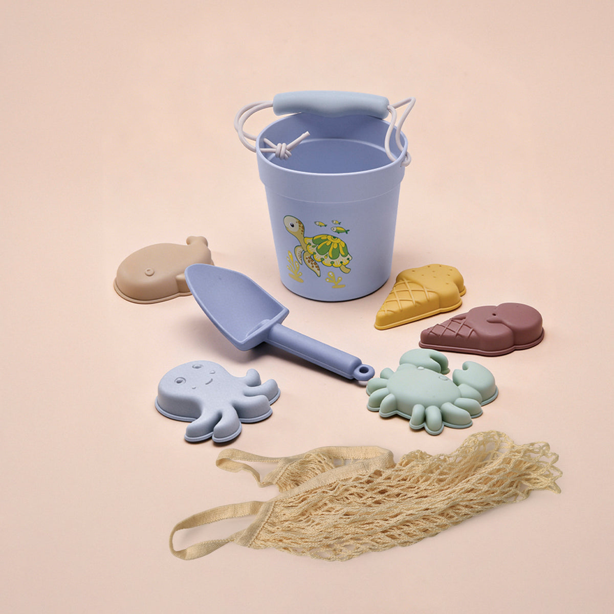 Set of beach toys including a blue bucket, spade, and various molds on a beige background