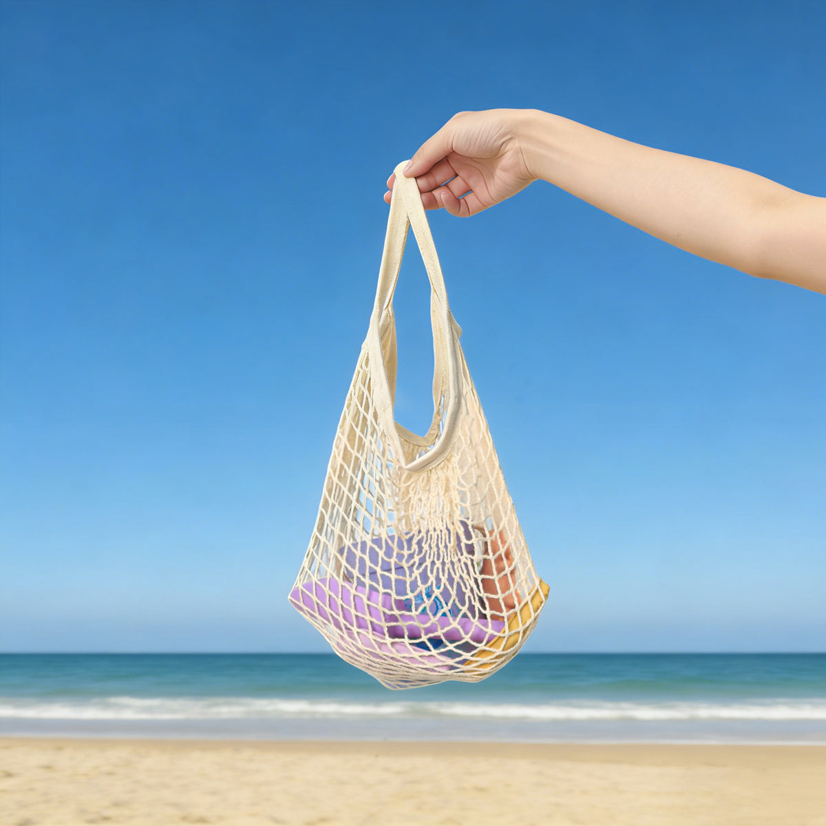 Hand holding a net bag with colorful items against a beach background