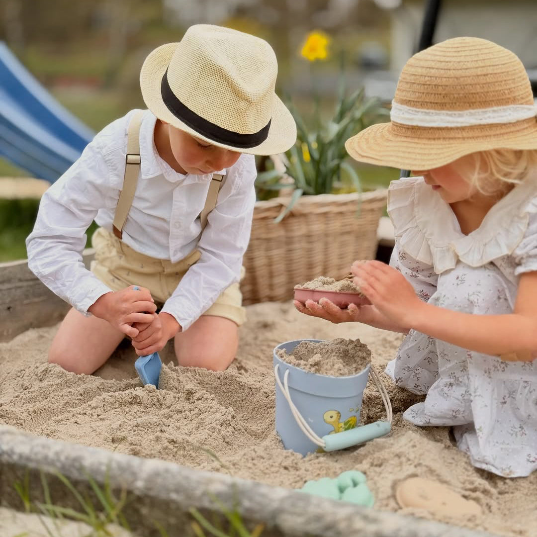 Two children playing in a sandbox with hats on