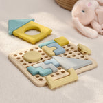 Colorful geometric shape sorting toy on a soft surface with a plush toy in the background 