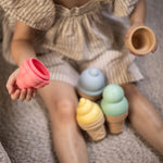 Child holding a pink silicone ice cream cone with more silicone ice cream cones on the ground.