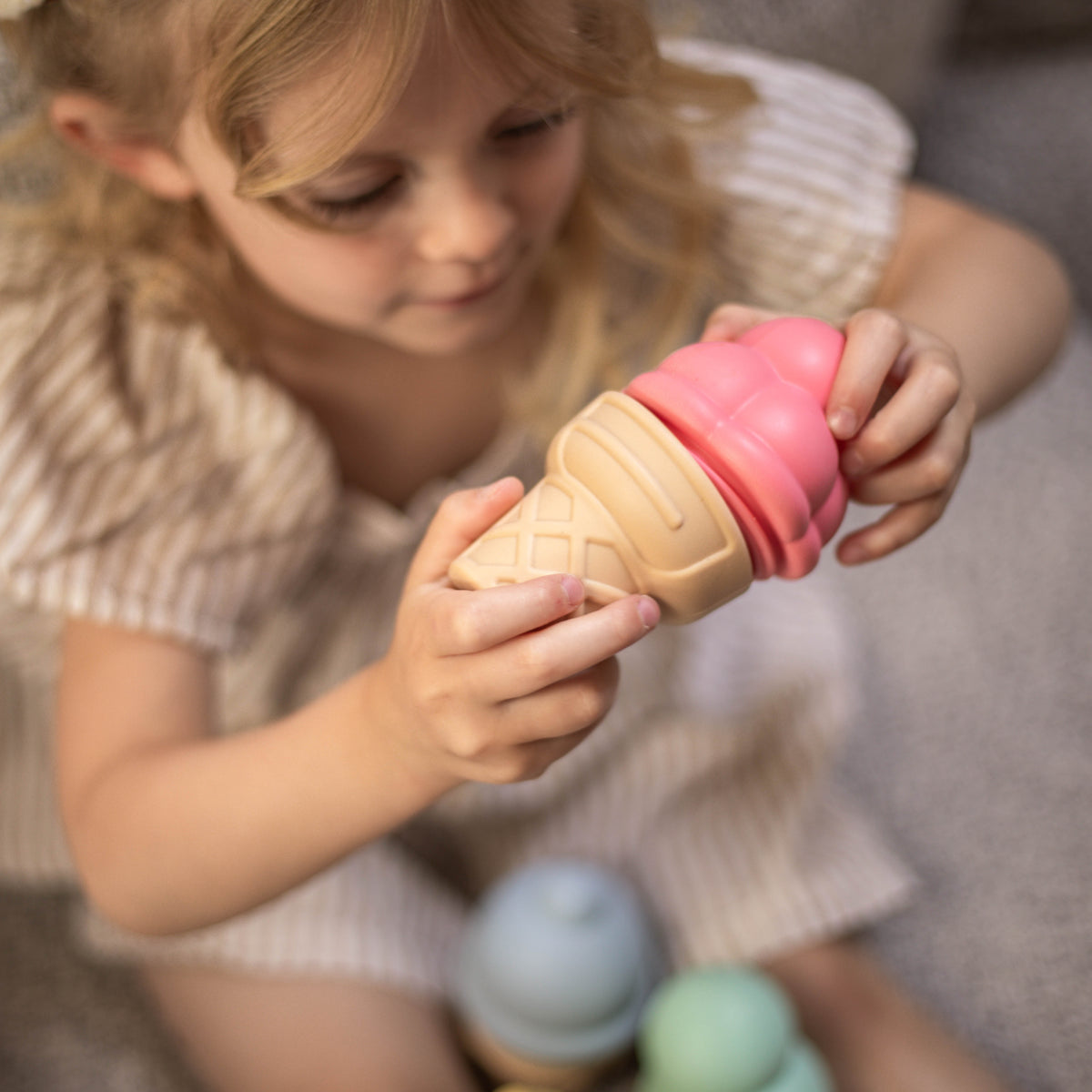 Child holding a toy ice cream cone with a pink scoop.