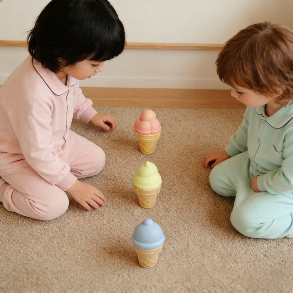 Two children playing with toy ice cream cones on a carpeted floor.
