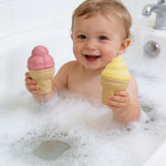 Child in a bathtub holding two ice cream-shaped toys.
