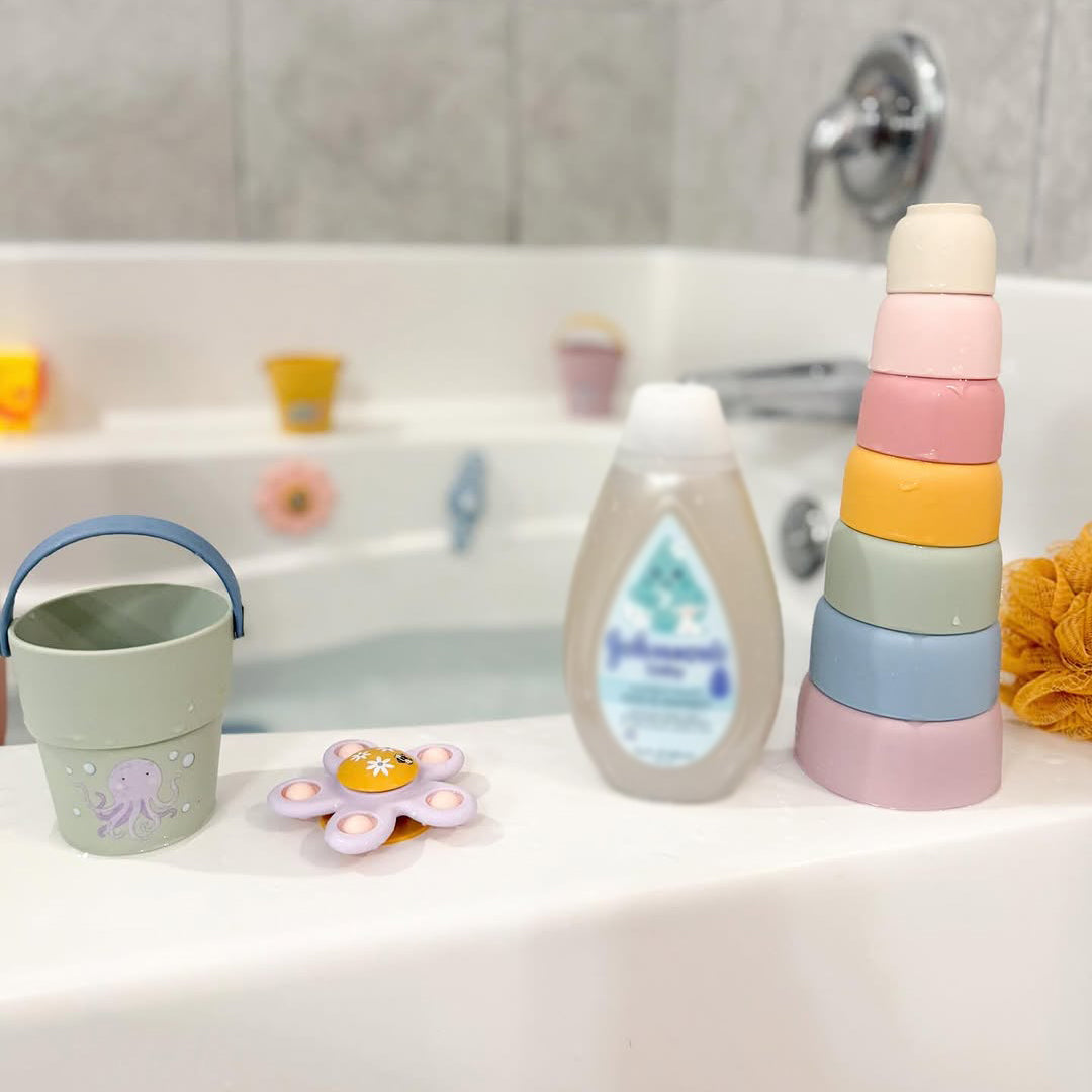 Bath time setup with a bottle, bucket, and toys on a bathtub ledge. 