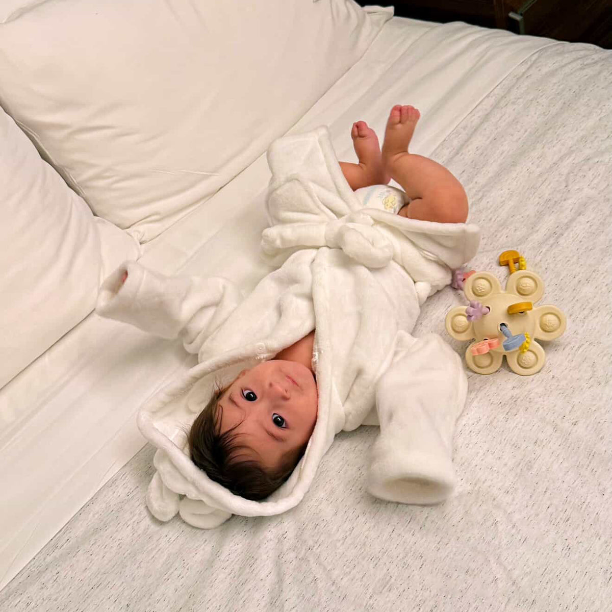 Newborn baby wrapped in a white blanket on a bed with a toy nearby