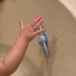 Child's hand reaching towards a blue shower handle on a beige wall. 