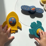 Colorful children's toys on a white surface with hands interacting with them. 