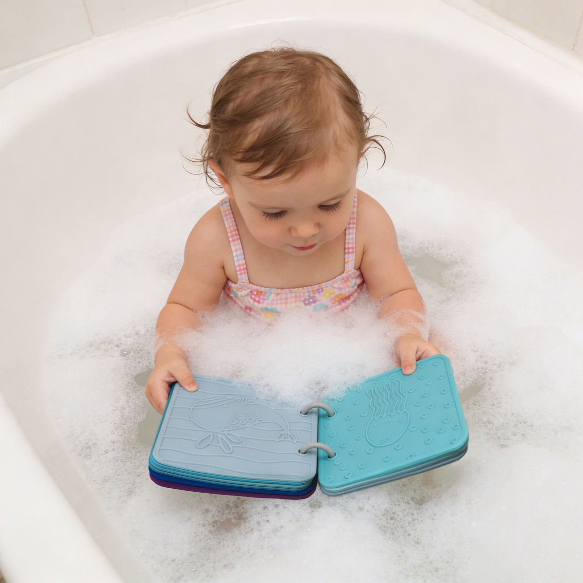 Child playing with a blue bath book in a bathtub filled with bubbles 