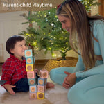 A toddler sits on a carpeted floor next to a woman, building a tower of colorful wooden blocks with numbers and shapes. A decorated Christmas tree with warm lights is in the background, and the text 'Parent-child Playtime' is visible at the top left.