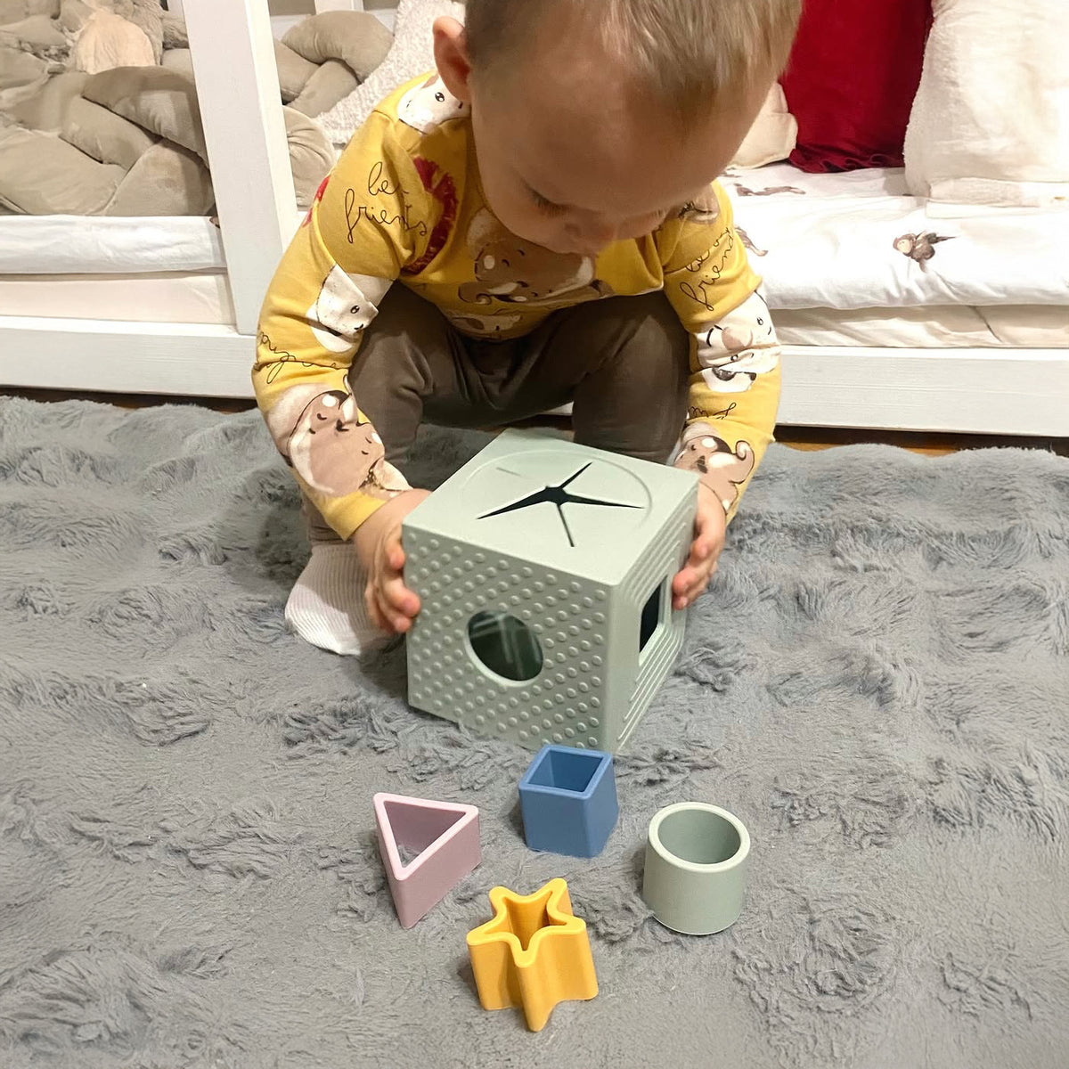 Child playing with a shape sorting toy on a carpeted floor.
