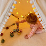 Child playing with blocks inside a cozy indoor play area with string lights.