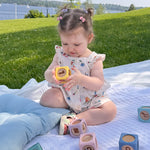 Child playing with blocks on a blanket outdoors by a lake