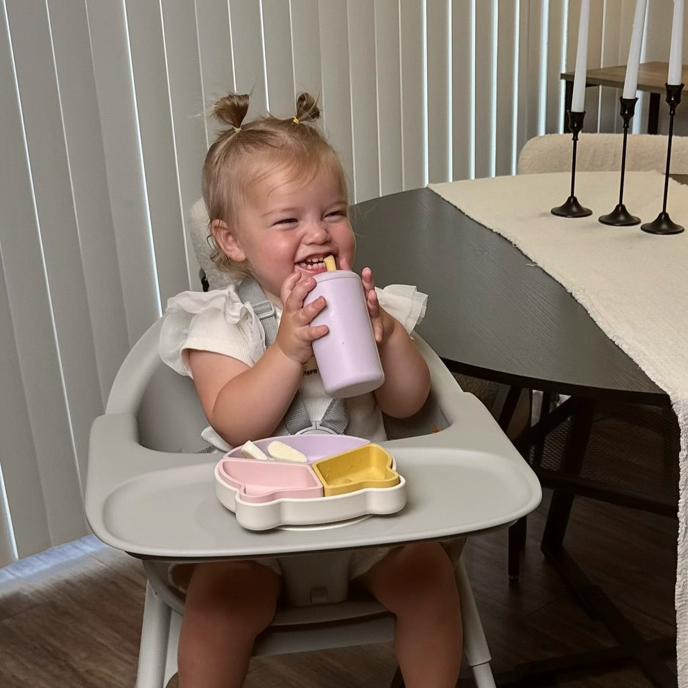 Child in a high chair with a pink cup and tray at a dining table. 