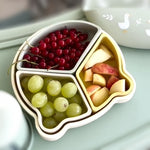 Fruit bowl with compartments containing grapes, apples, and red berries on a light surface. 