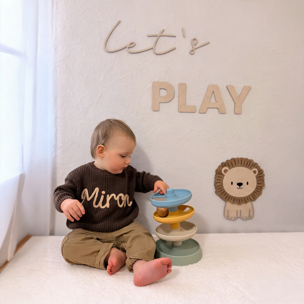 Child playing with a toy in a room with a 'Let's Play' sign on the wall.