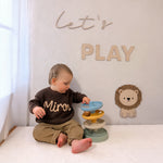 Child playing with a toy in a room with a 'Let's Play' sign on the wall.