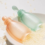 Two gradient bottles, one orange and one green, on a white surface with small pearls.