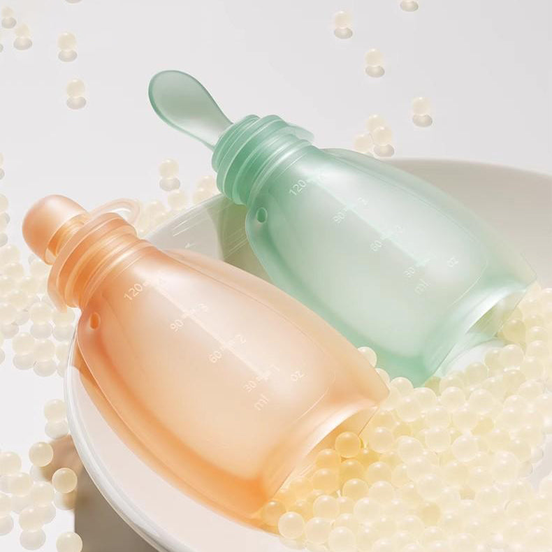 Two gradient bottles, one orange and one green, on a white surface with small pearls.