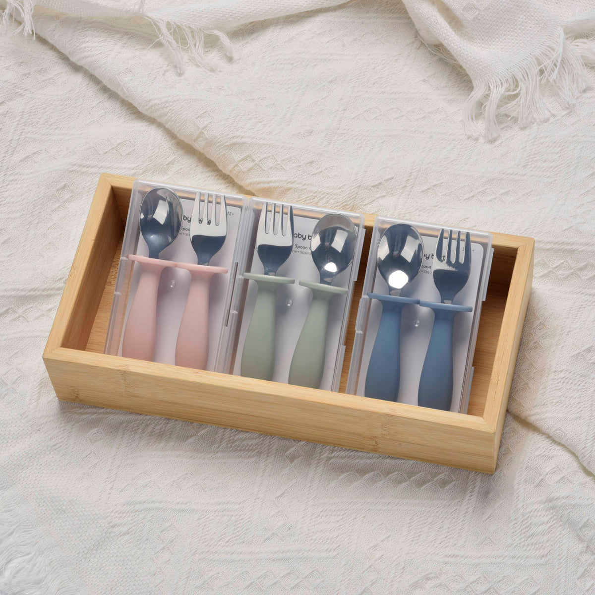 Set of colorful cutlery in a wooden box on a textured white surface