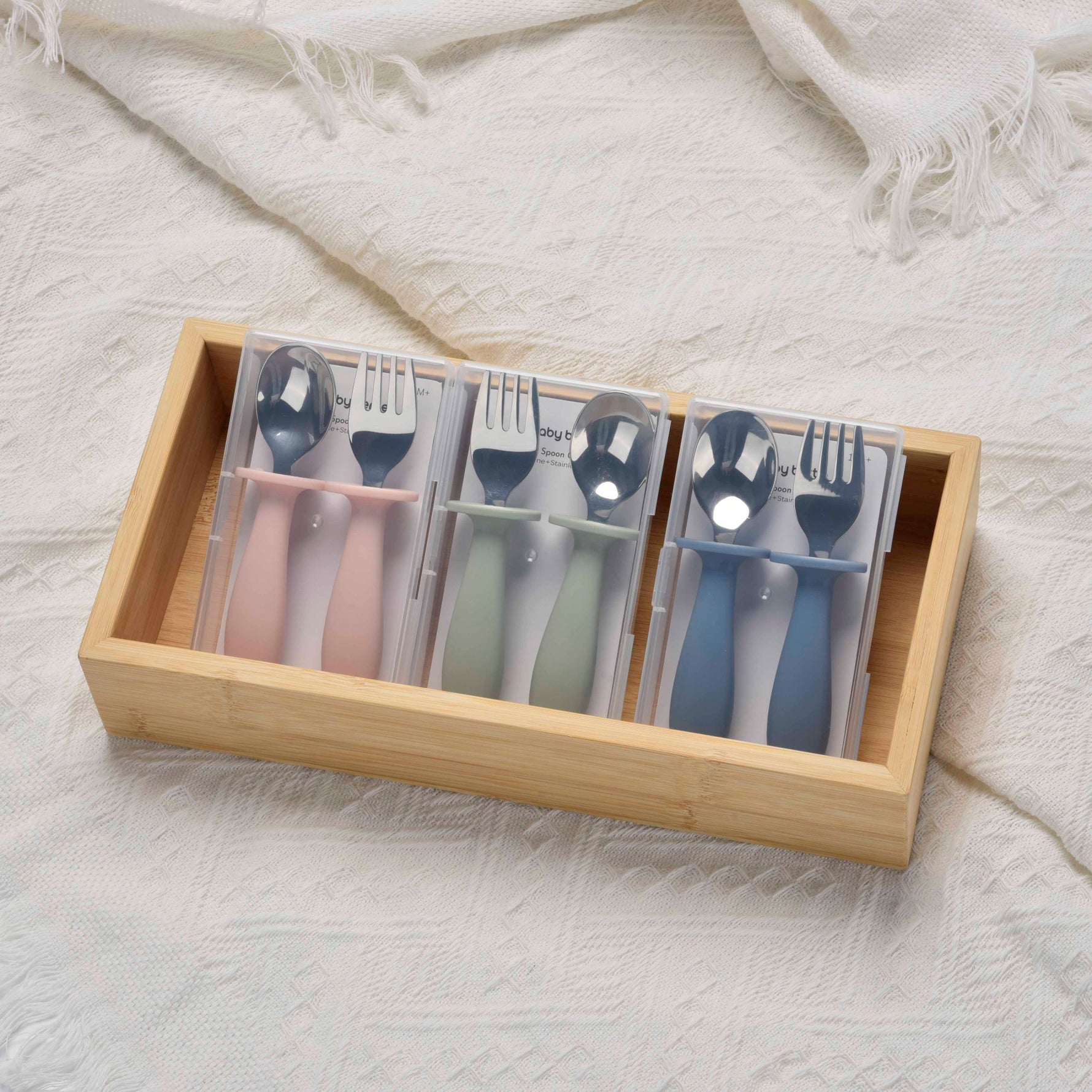 Set of colorful cutlery in a wooden box on a textured white surface