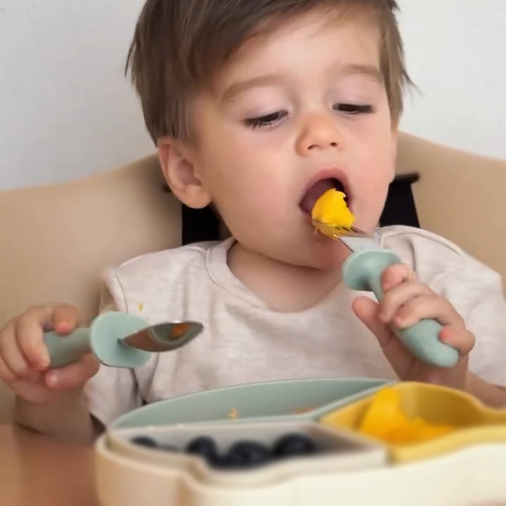 Child eating with a spoon and fork, sitting in a high chair 