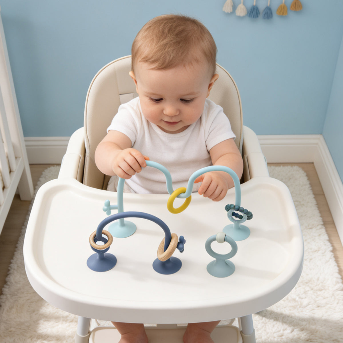 Baby sitting in a high chair with a colorful toy, in a room with light blue walls and white furniture.