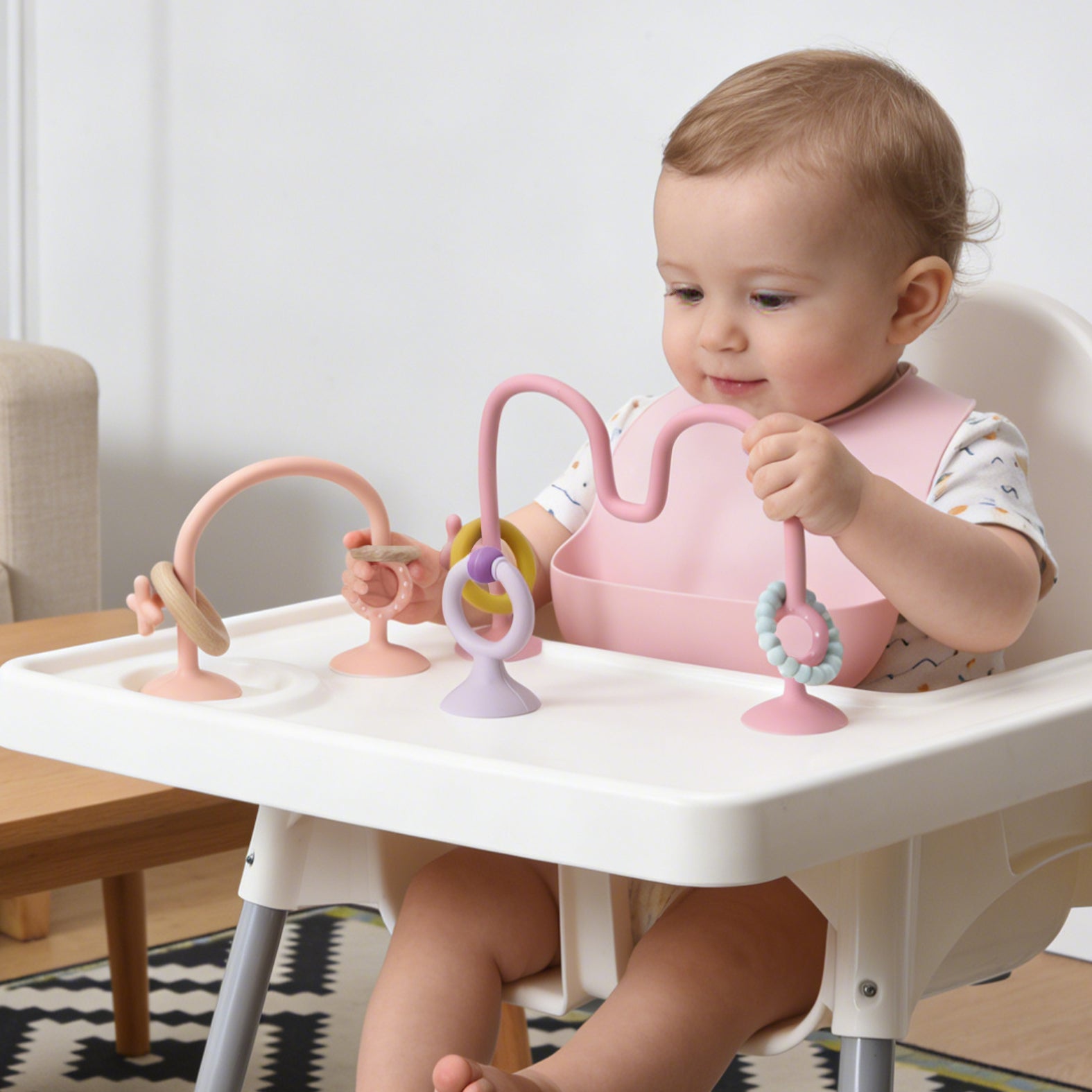 Baby sitting in a high chair playing with colorful baby toys.