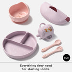 A 6-piece baby feeding set for starting solids, including a pink suction bowl, a lavender divided plate, a small sippy cup, a lid, a spoon, and a fork, arranged on a light gray background with text at the bottom.