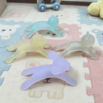 Four silicone teething toys in different colors on a patterned surface.