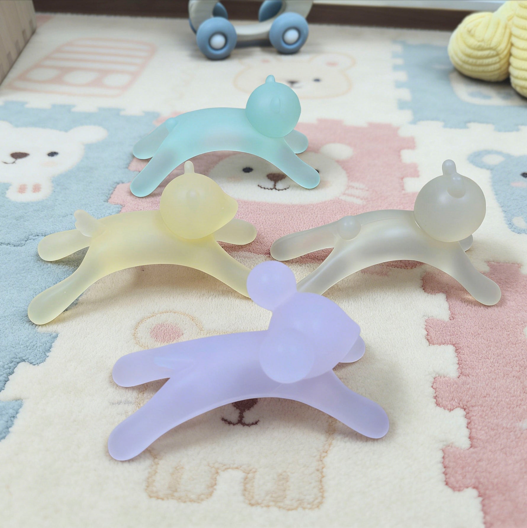 Four silicone teething toys in different colors on a patterned surface.