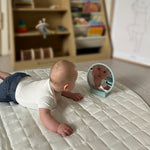Baby lying on a mattress looking at its reflection in a small mirror. 
