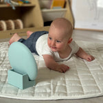 Baby lying on a mattress with a mirror stand in a room setting 