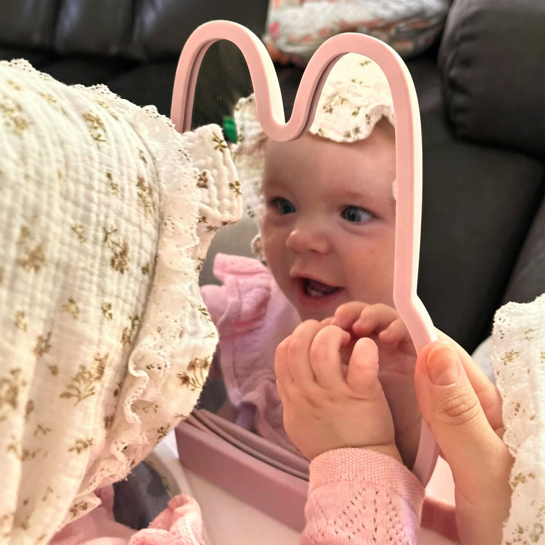 Baby looking at a pink mirror with bunny ears, wearing a pink outfit. 