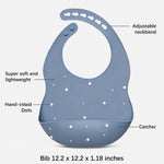A blue baby bib with white and yellow dots, shown with callout labels pointing to its features: adjustable neckband, super soft and lightweight, hand-inlaid dots, catcher, and size 12.2 x 12.