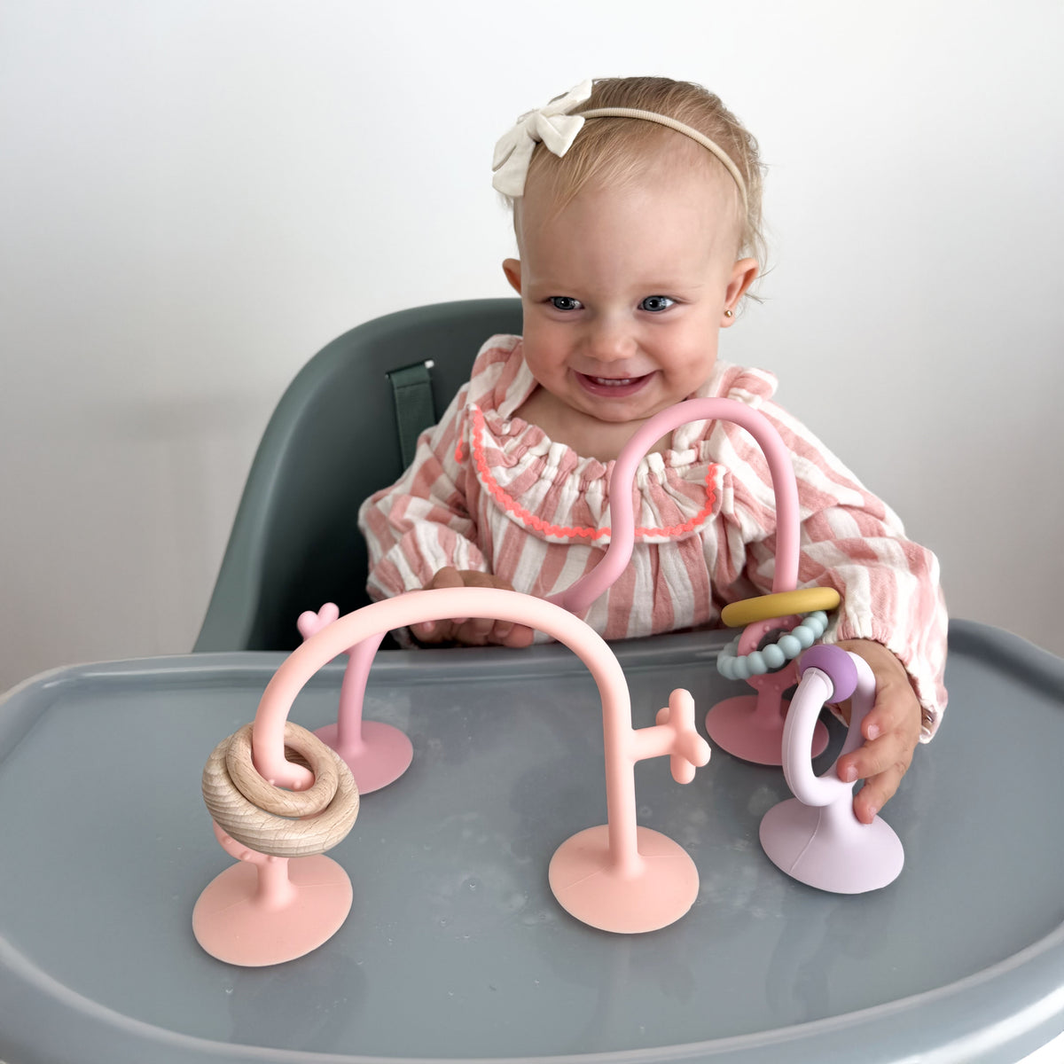 Baby sitting in a high chair with pink baby toys 