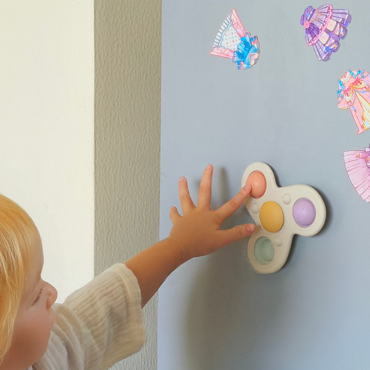 Child interacting with a colorful toy on a light gray wall with decorative stickers.